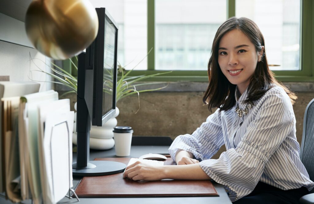 Chinese woman at a computer in an office smiling to camera