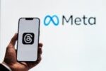 A hand holding a smartphone showing the Threads app with Meta logo in the background.